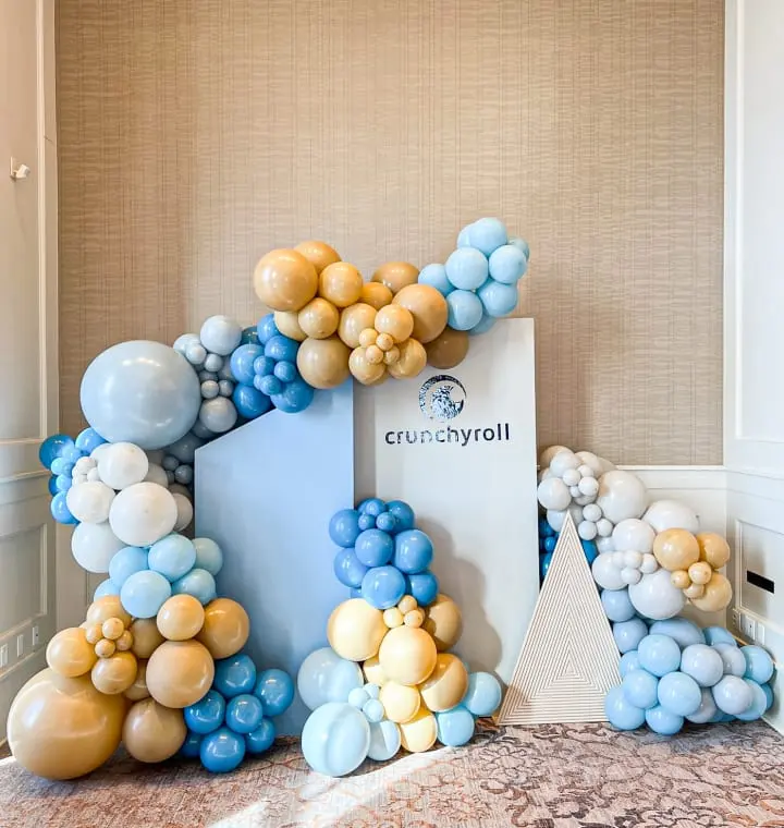 a balloon arch with blue, gold, and white balloons in the shape of the letter e on a carpeted floor