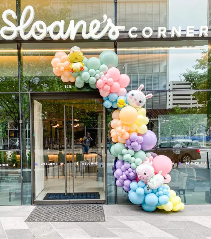a bunch of balloons that are in front of a store front door that says sloan's corner on the front of the building