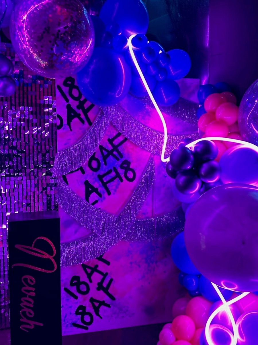 The image depicts a vibrant and colorful display of various objects, including a disco ball, neon lights, and handwritten text against a dark background, creating an energetic and visually striking atmosphere.