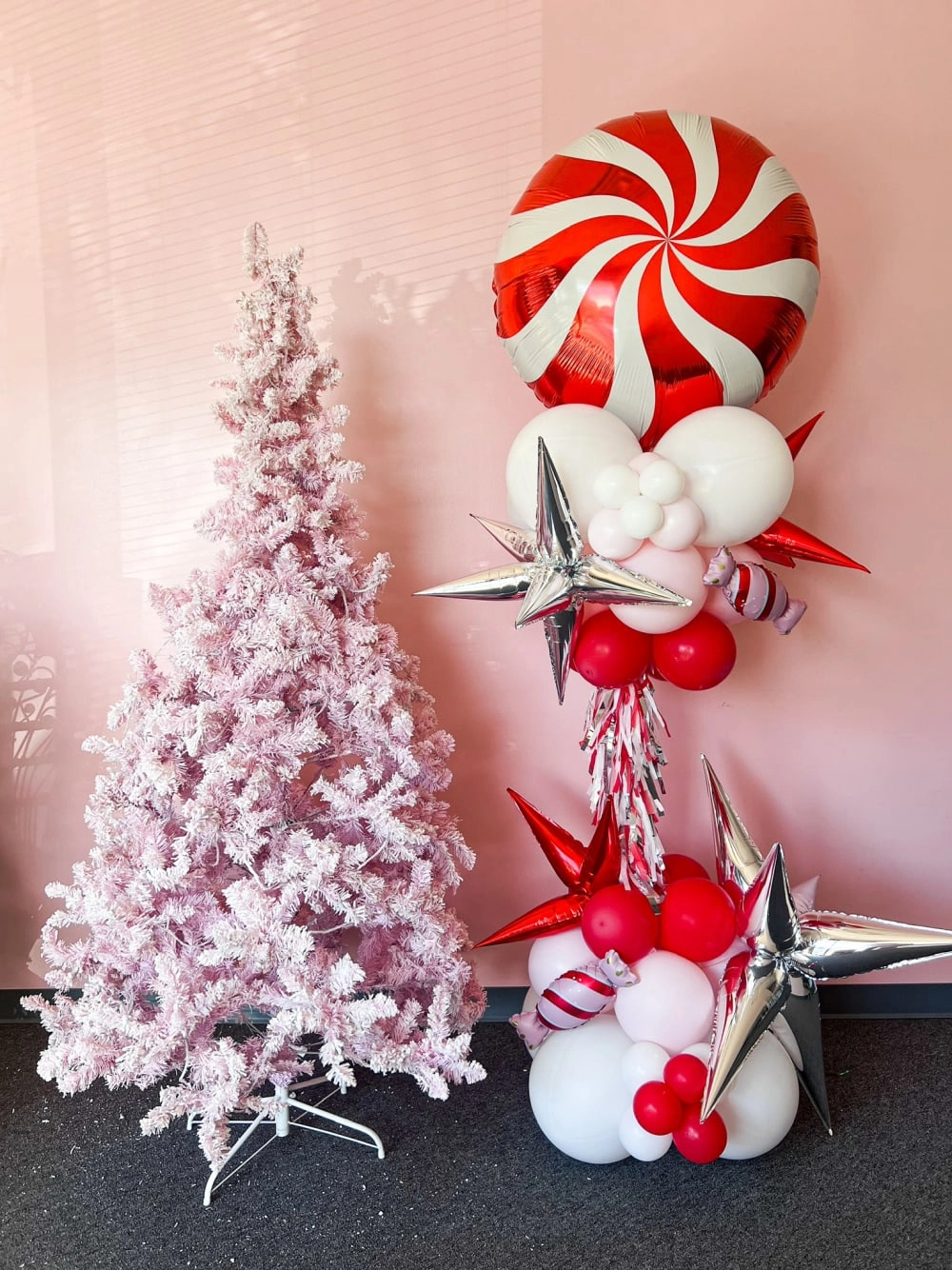 The image depicts a festive holiday scene, with a flocked white Christmas tree in the background and various decorative elements in the foreground, including a large red and white peppermint-striped ornament, white and red ornaments, and a star-shaped decoration.