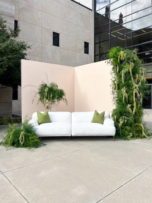 a white couch sitting on top of a cement floor next to a tall planter filled with green plants