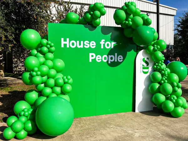 a green house for people sign with balloons in the shape of a tree and a bunch of green balls