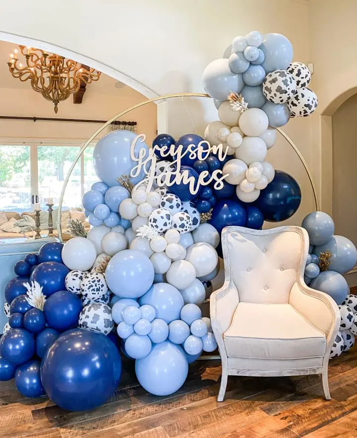 a balloon arch with blue and white balloons and a white chair in front of it with a happy birthday sign on it