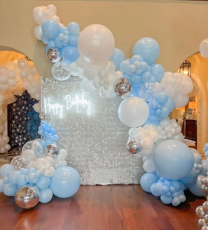 a balloon arch with blue and white balloons on a wooden floor in front of a mirror with a happy birthday message on it