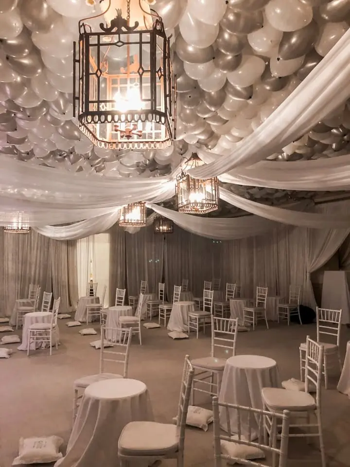 a banquet hall decorated with balloons and white tables and chairs and a chandelier hanging from the ceiling