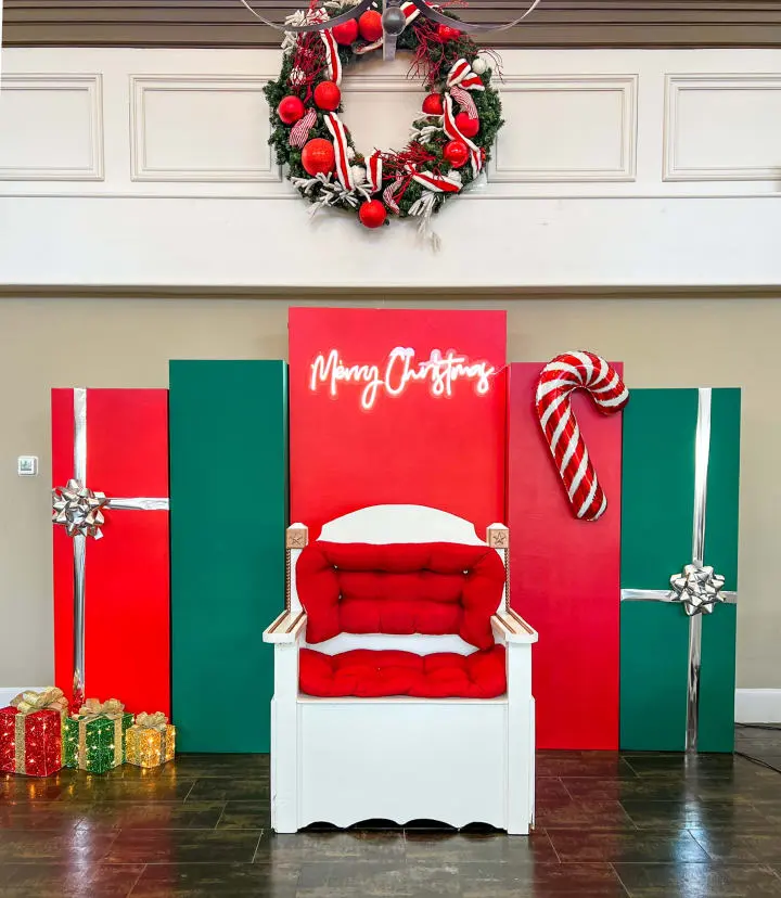 a red and white chair sitting in front of a christmas wreath on a red and green wall next to a red and white chair
