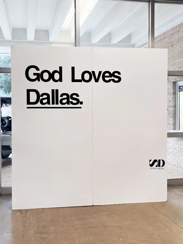 a large white sign that says god loves dallas in black lettering on a white wall in a building