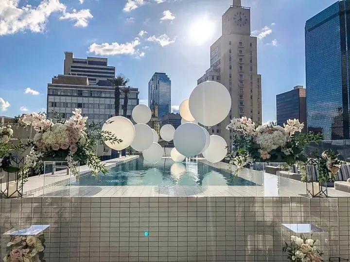 a swimming pool with balloons and flowers in the middle of it and a city skyline in the background with skyscrapers in the background