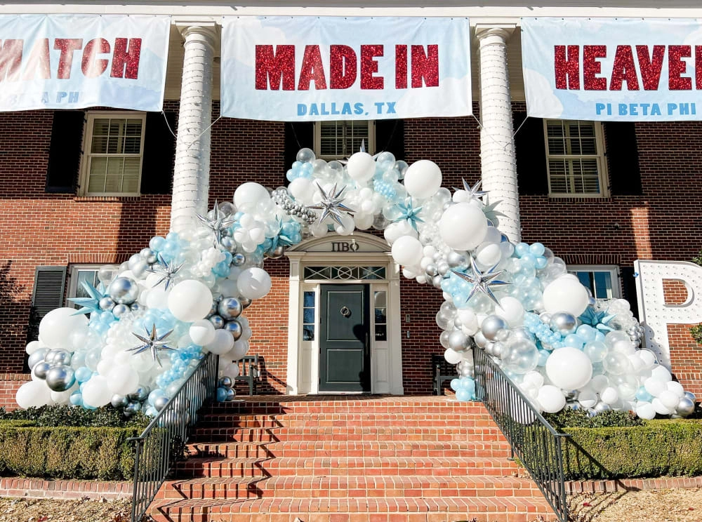 A brick building with a large "Made in Heaven" sign on the front, decorated with a colorful balloon arch and other festive elements on the steps leading up to the entrance.