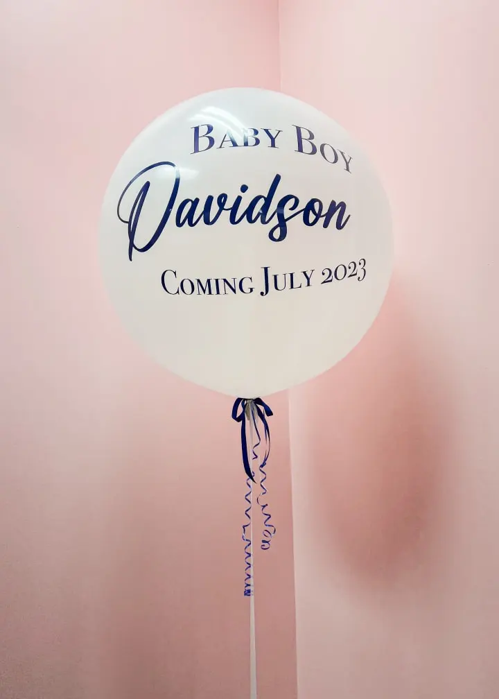 a balloon with a baby boy name hanging from the ceiling of a room with pink walls and a blue ribbon on the bottom of the balloon