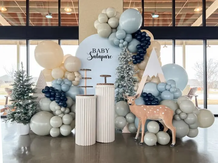 a baby shower backdrop with balloons and a deer in front of a sign and a deer in front of it