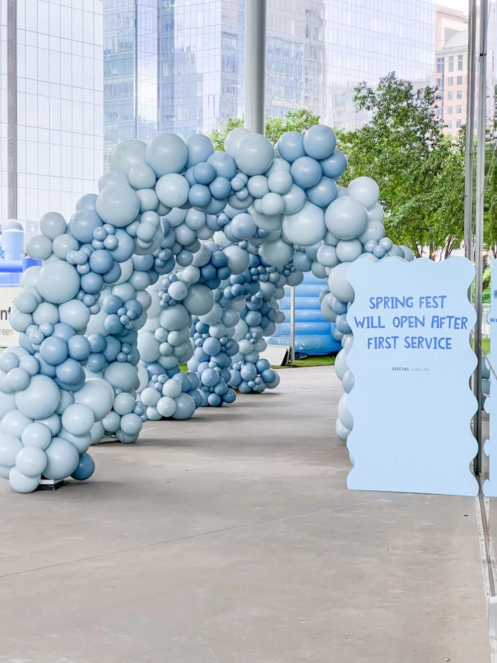 a bunch of balloons are lined up in a row on a sidewalk in front of a building with a sign that says springfest will open after first service