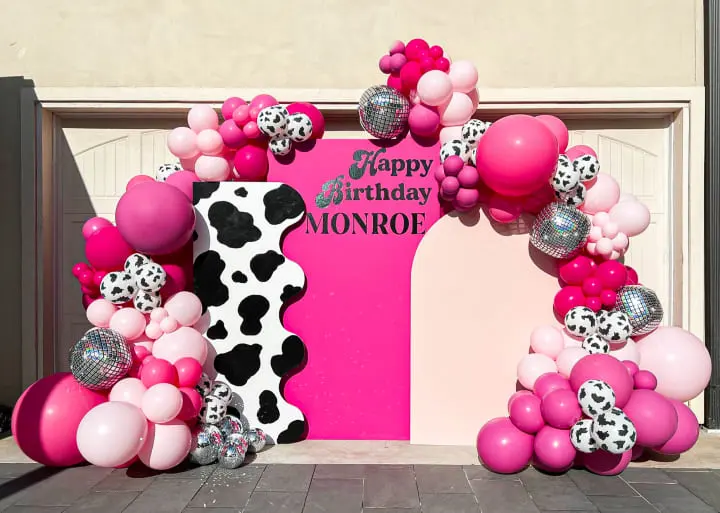 a pink and black decorated birthday arch with balloons and a cow print number one on the front of the arch