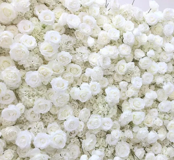 a bunch of white flowers that are in a vase on a table in front of a wall of white flowers