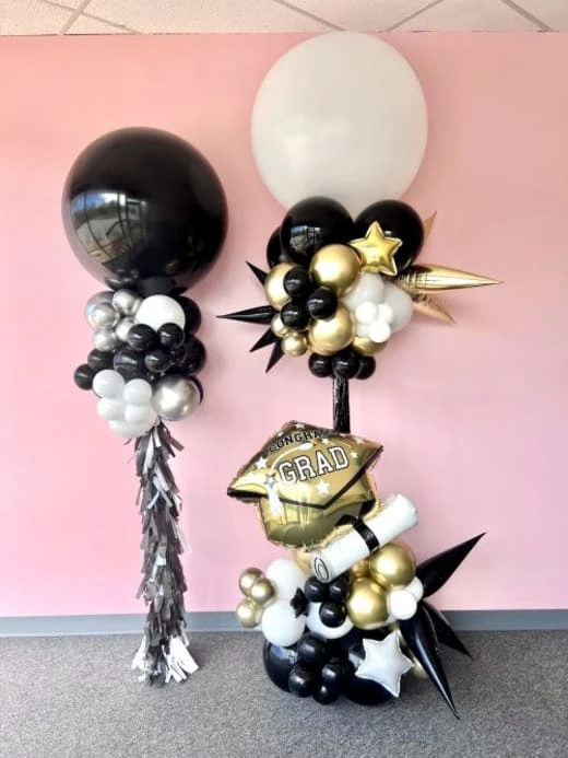 a balloon display with black, white and gold balloons and a black and gold graduation cap and tassel