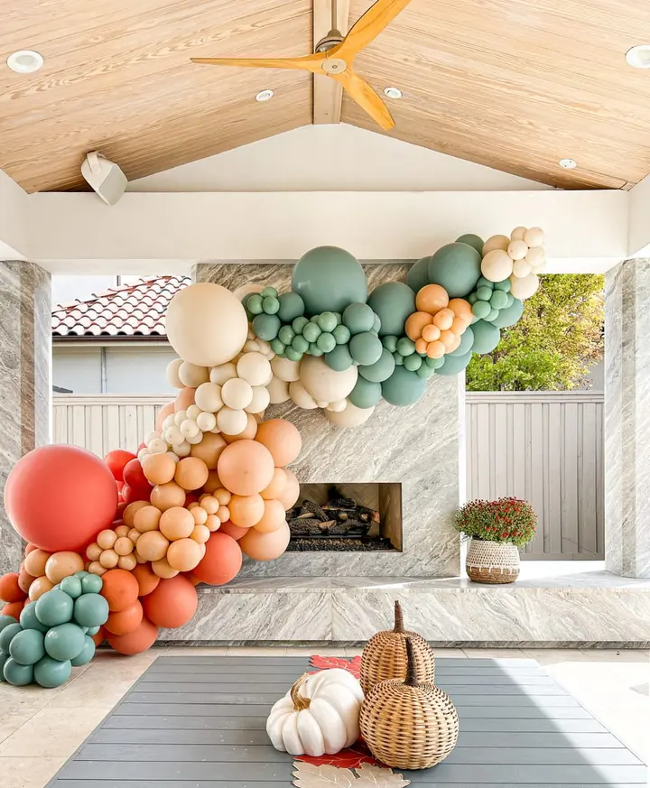 A vibrant and whimsical balloon arch in shades of green, orange, and white adorns the interior of a cozy, rustic-style room, complemented by a fireplace and various decorative elements.