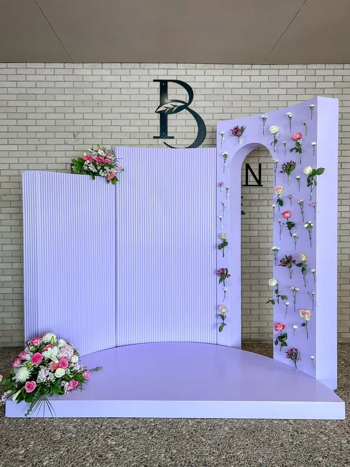 A decorative backdrop with floral arrangements, a raised platform, and a brick wall with the letters "PB" and "N" displayed.