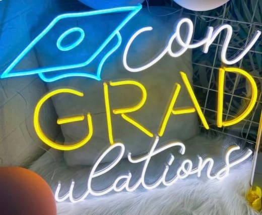 a neon sign that reads congratulations grad on a white furnishing next to balloons