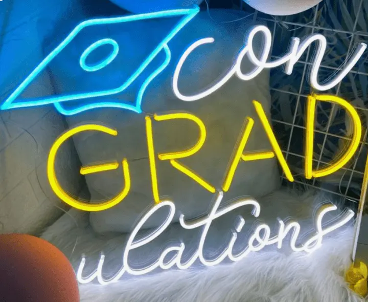 a neon sign that reads zoom grad questions on a white furnishing next to balloons and a stuffed animal
