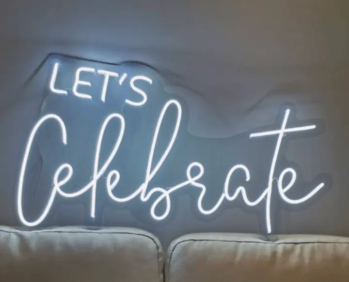 a neon sign that says let's celebrate on a wall above a couch in a room with white walls