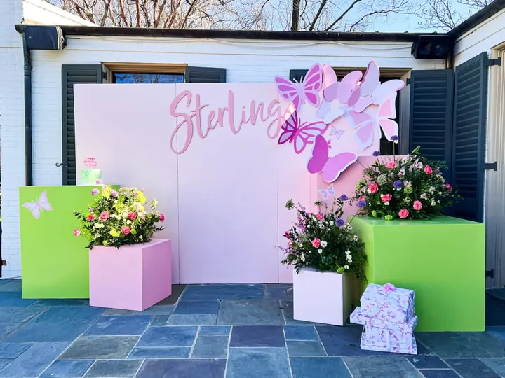 A colorful and vibrant outdoor display featuring a large pink butterfly decoration, potted plants, and a sign that says "Sterling".