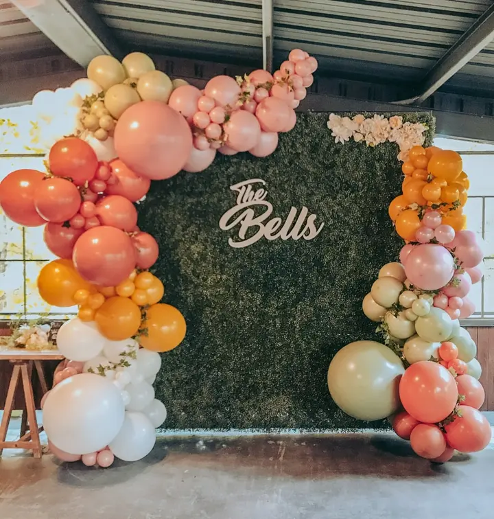 A vibrant and colorful balloon arch surrounds a large black backdrop with the text "The Bells" prominently displayed, creating a visually striking and festive scene.