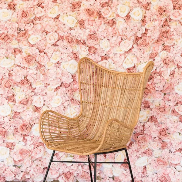 a wicker chair sitting in front of a wall of pink and white flowers with a black metal frame