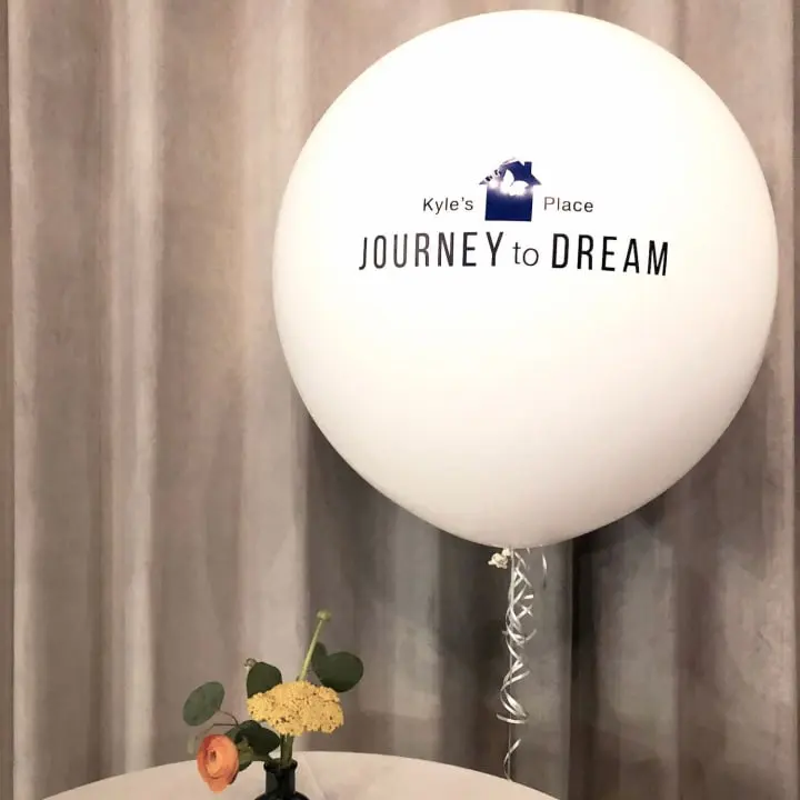 a vase with flowers on top of a table with a balloon in the shape of a house and a sign that says journey to dream