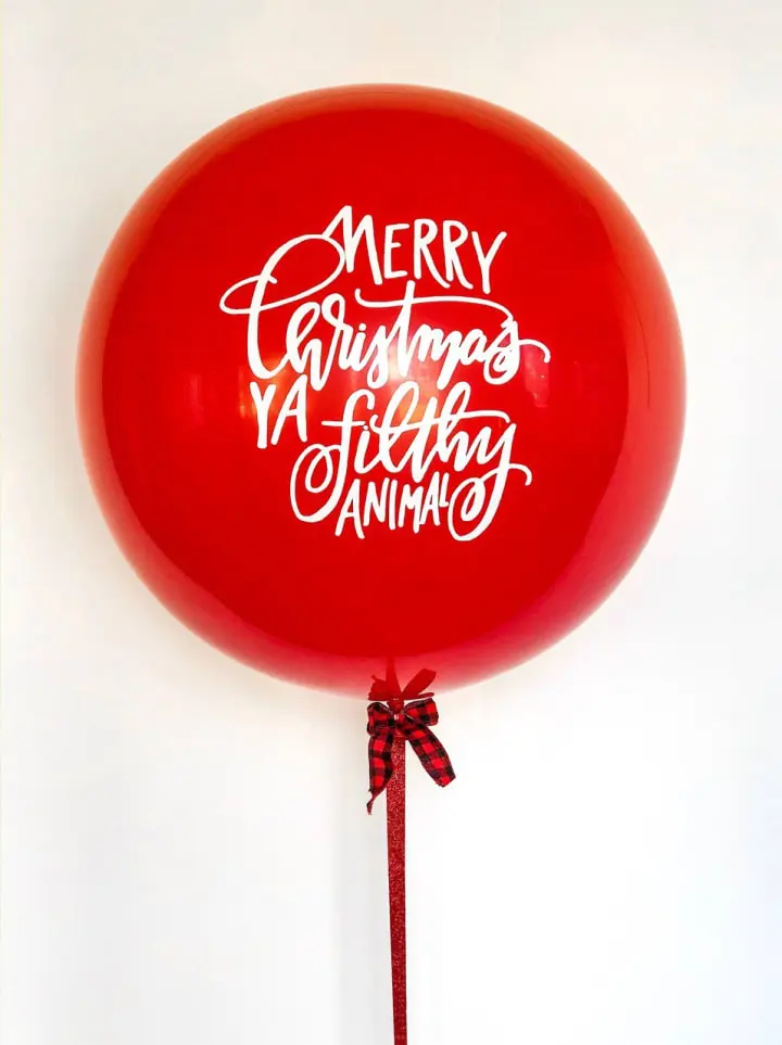 a large red balloon with a merry christmas message on it's side and a red ribbon tied around the bottom of the balloon