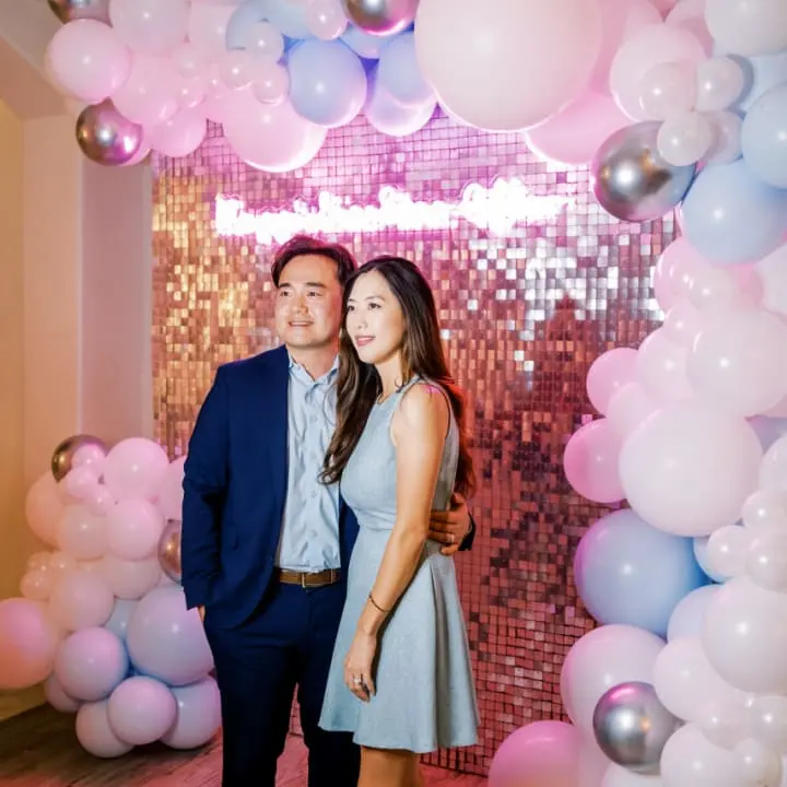 a man and a woman standing in front of a backdrop of balloons and streamers with a backdrop of balloons