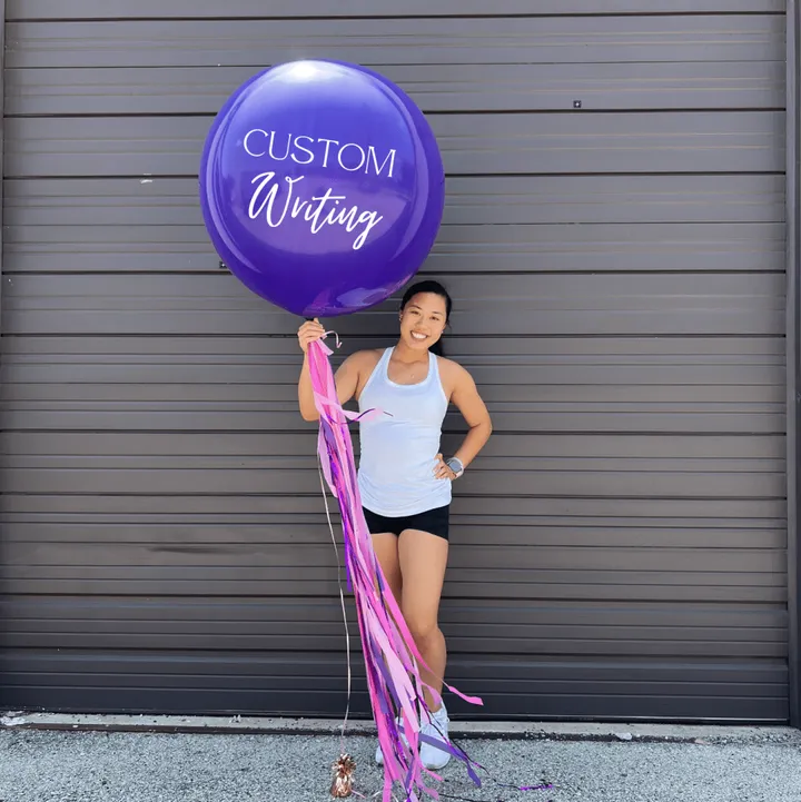 a woman holding a purple balloon that says custom writing on it and a pink streamer in front of her