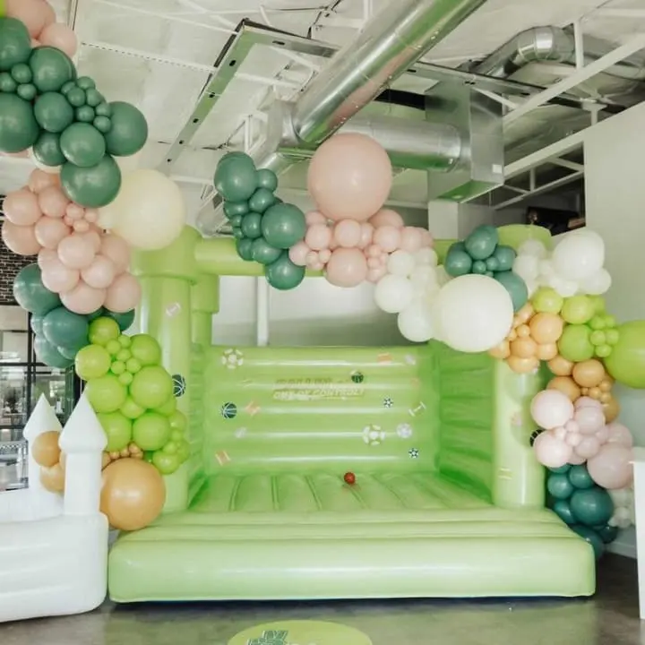 a green inflatable arch with balloons and a bunch of white and green balloons hanging from the ceiling