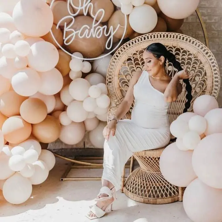 a woman in a white dress sitting in a chair surrounded by balloons and a sign that says oh baby