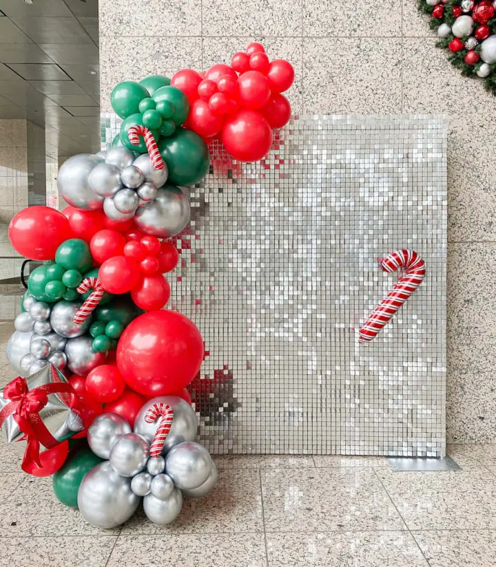 a bunch of balloons and a candy cane on the floor of a building with a mosaic wall in the background