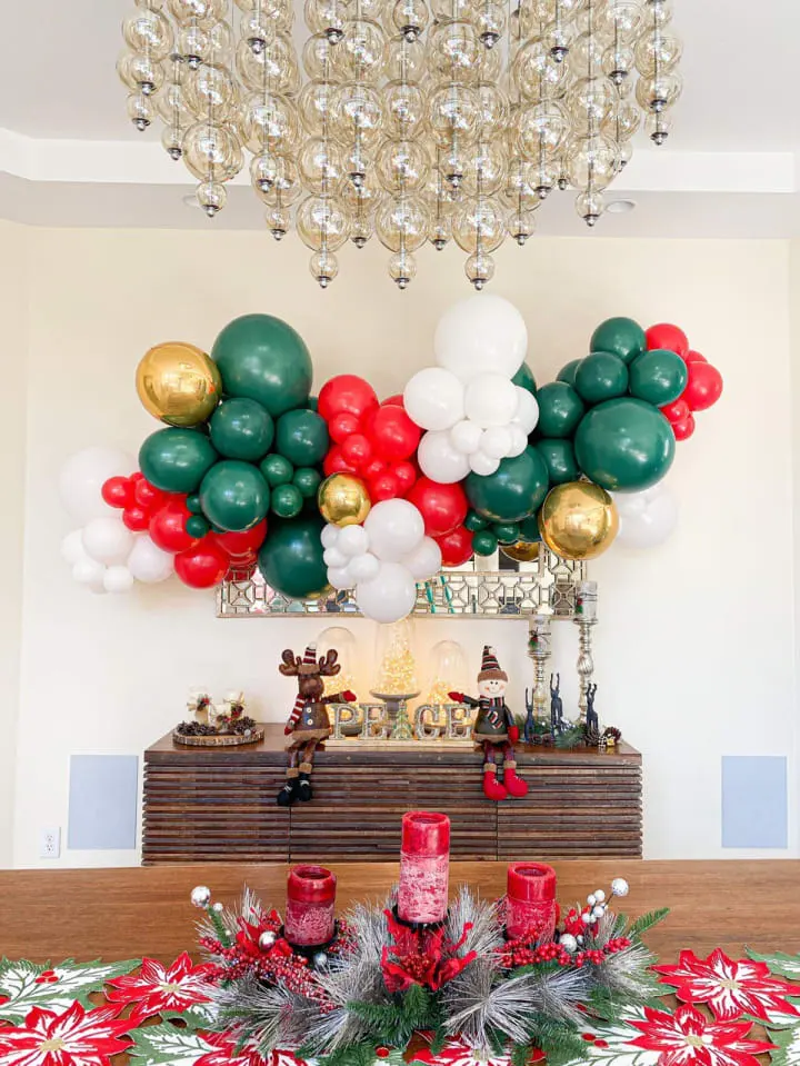 a table with a bunch of balloons on top of it next to a christmas table cloth and a chandelier