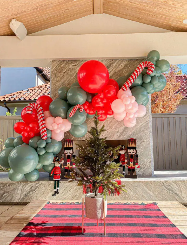 a large balloon arch is decorated with red, white and green balloons and a christmas tree in a vase