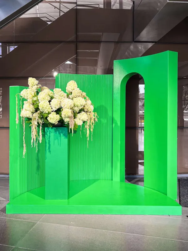 The image features a large green wall with a display of white flowers, including a large bouquet of flowers, and a vase filled with flowers.