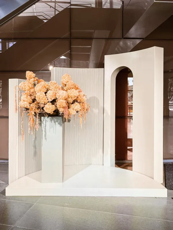A large vase filled with flowers is placed on a table in a room, with a doorway visible in the background.