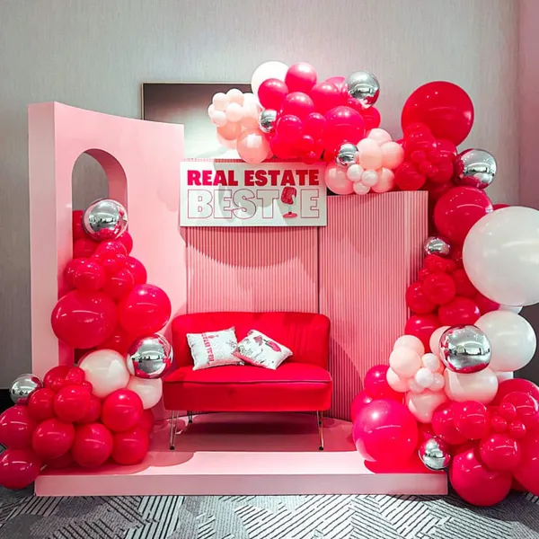 The image features a room with a red couch and a pink wall, decorated with balloons and a large pink heart.