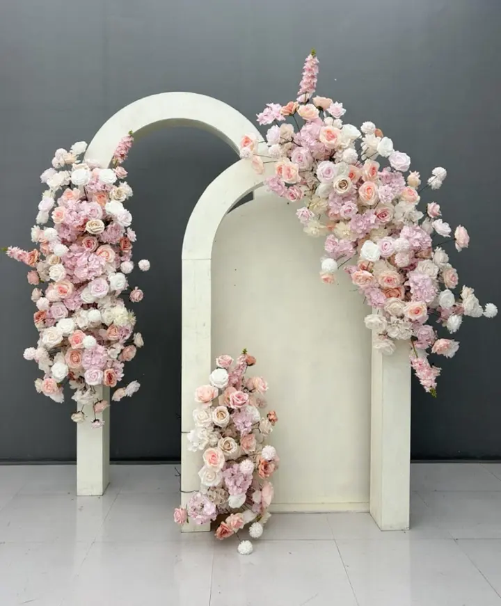 A serene and elegant floral display featuring delicate pink and white flowers cascading over a minimalist white architectural structure against a dark gray background.