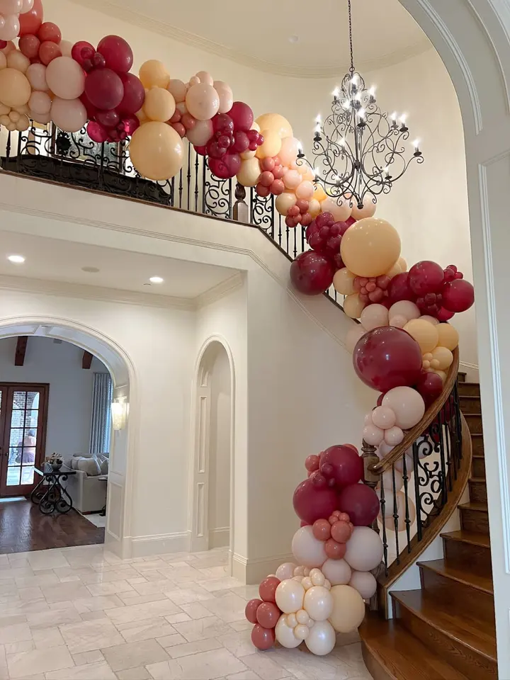 A grand staircase adorned with a vibrant balloon arch in shades of red, pink, and white, leading to a spacious and elegantly decorated interior.