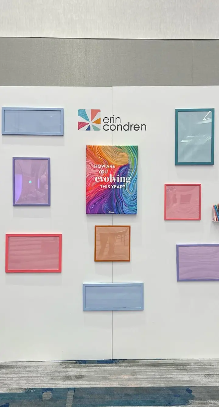 A white wall display featuring various colorful frames, including the Erin Condren logo, and a book titled "Evolving the Mind".