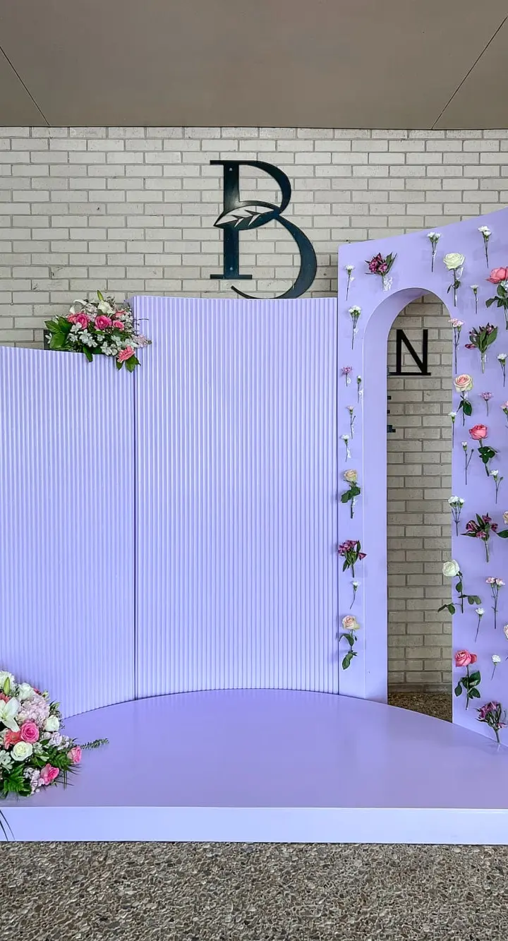 A decorative backdrop with floral arrangements, a raised platform, and a brick wall with the letters "PB" and "N" displayed.