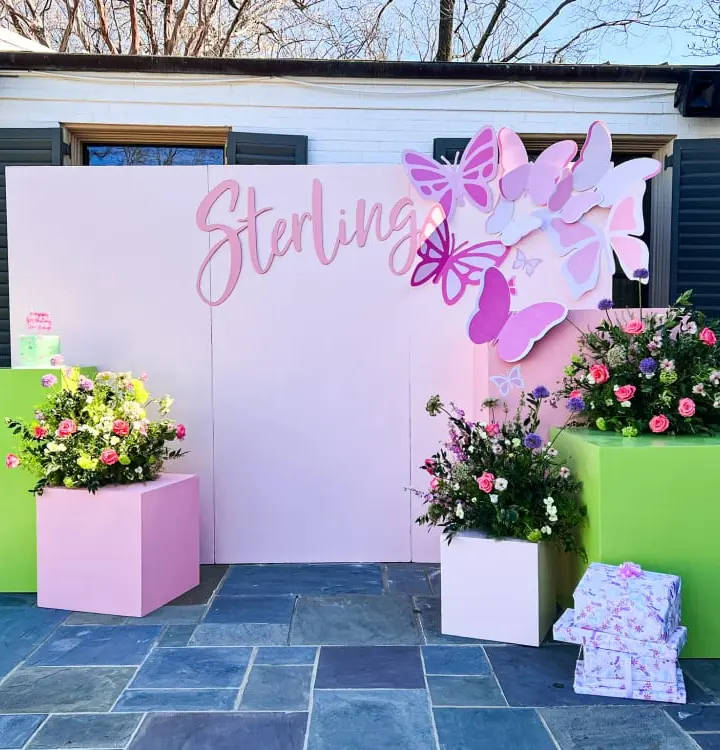 A colorful and vibrant outdoor display featuring a large pink butterfly decoration, potted plants, and a sign that says "Sterling".