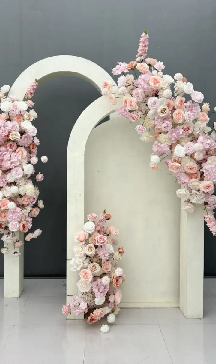 A serene and elegant floral display featuring delicate pink and white flowers cascading over a minimalist white architectural structure against a dark gray background.